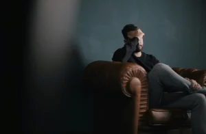 Zasmucony mężczyzna siedzi w fotelu, trzymając się za czoło.